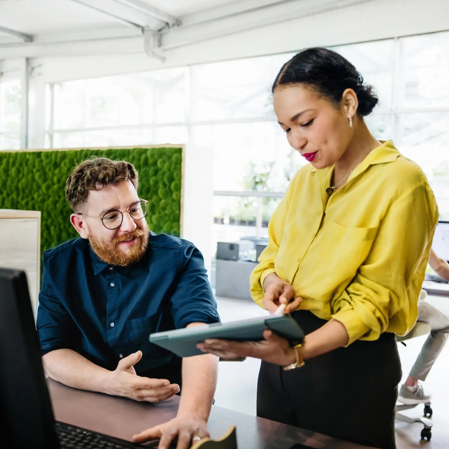 Ein Mann und eine Frau sind im Büro und schauen gemeinsam auf ein Tablet