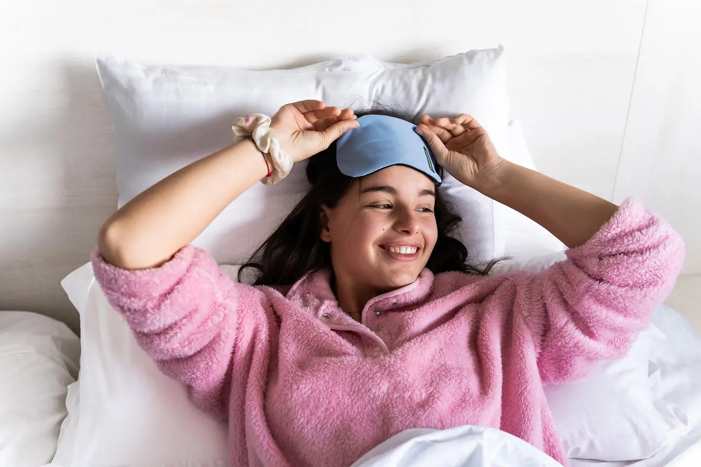 Eine junge Frau wacht auf und nimmt ihre Schlafmaske ab