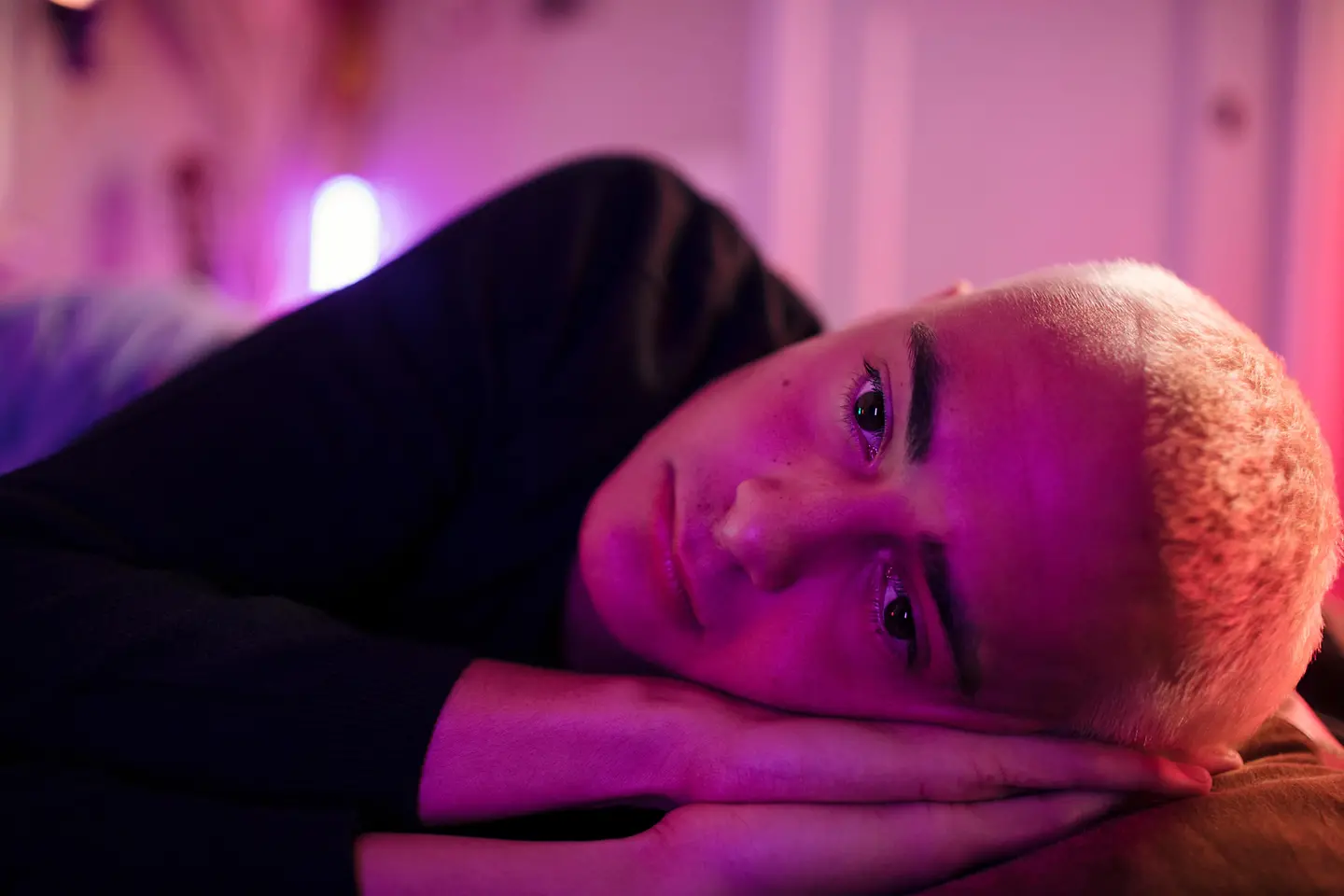 Junger Mann mit kurzen Haaren liegt im Dunklen im Bett und guckt depressiv