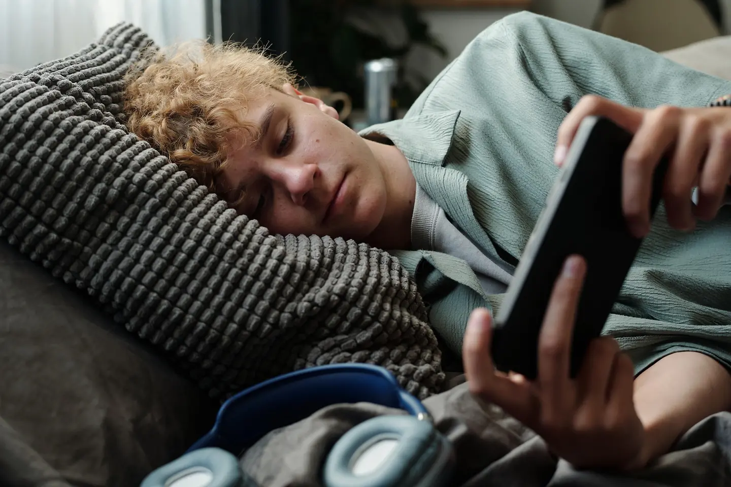 Jugendlicher liegt im Bett und schaut auf sein Handy