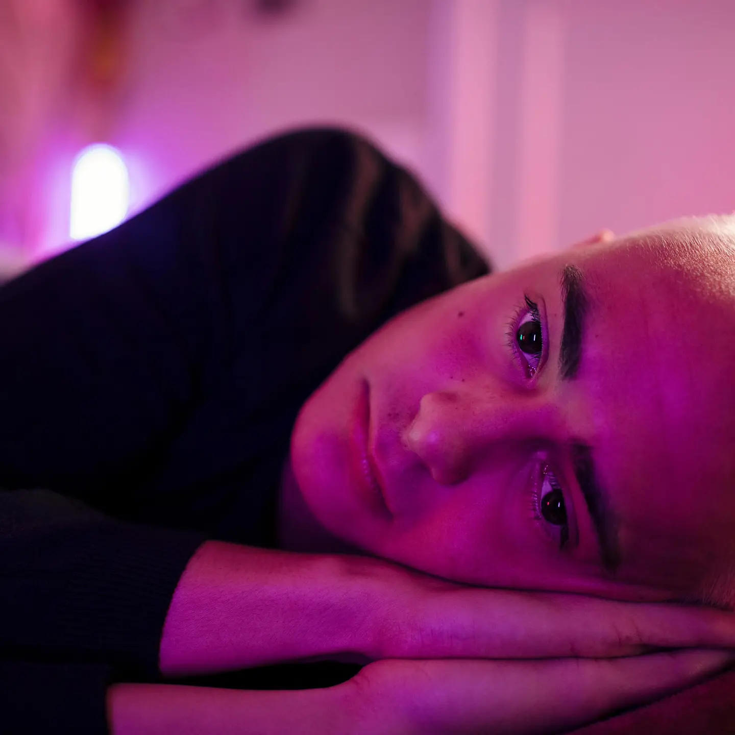 Junger Mann mit kurzen Haaren liegt im Dunklen im Bett und guckt depressiv