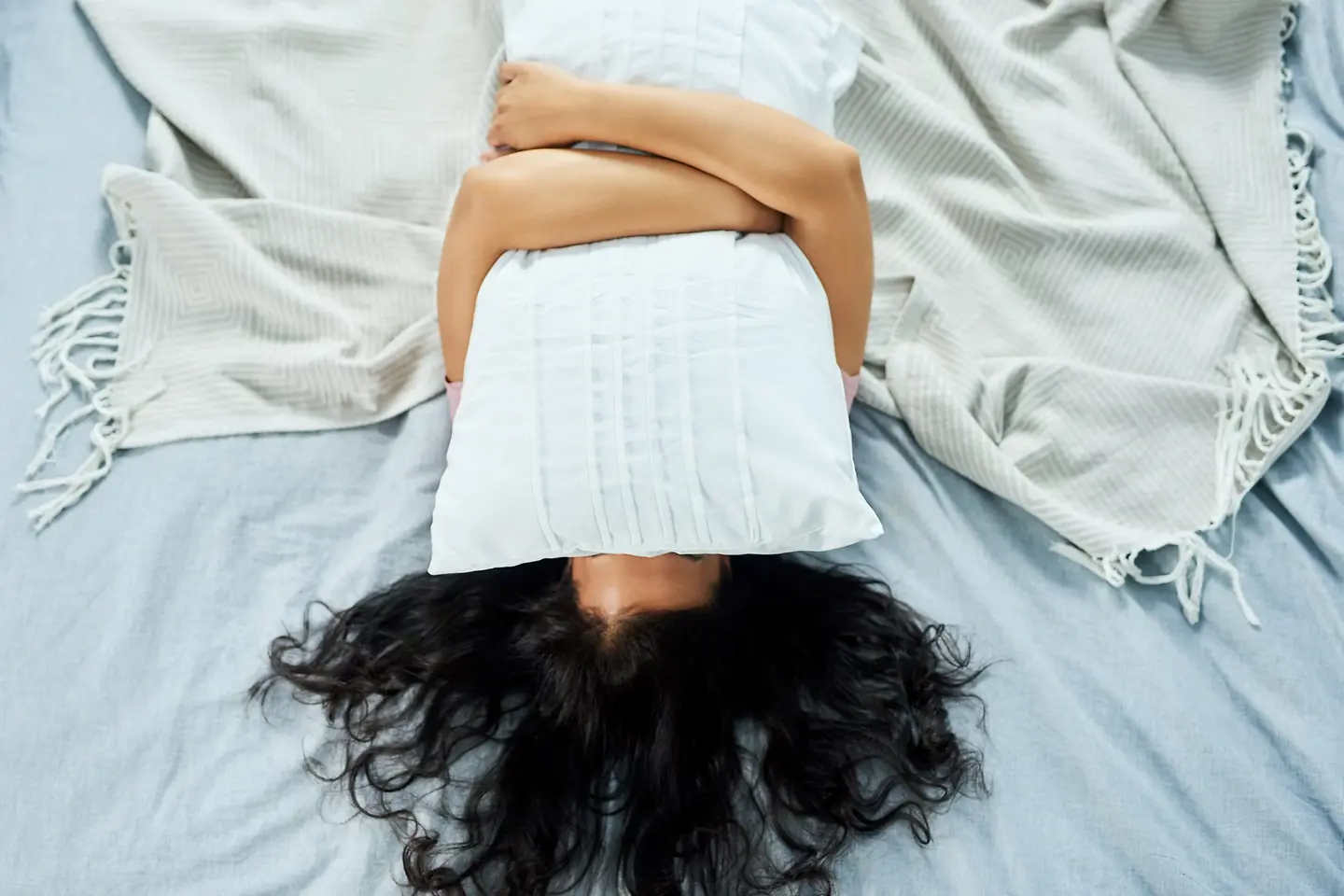 Frau liegt im Bett und hält sich ein Kissen vor ihr Gesicht
