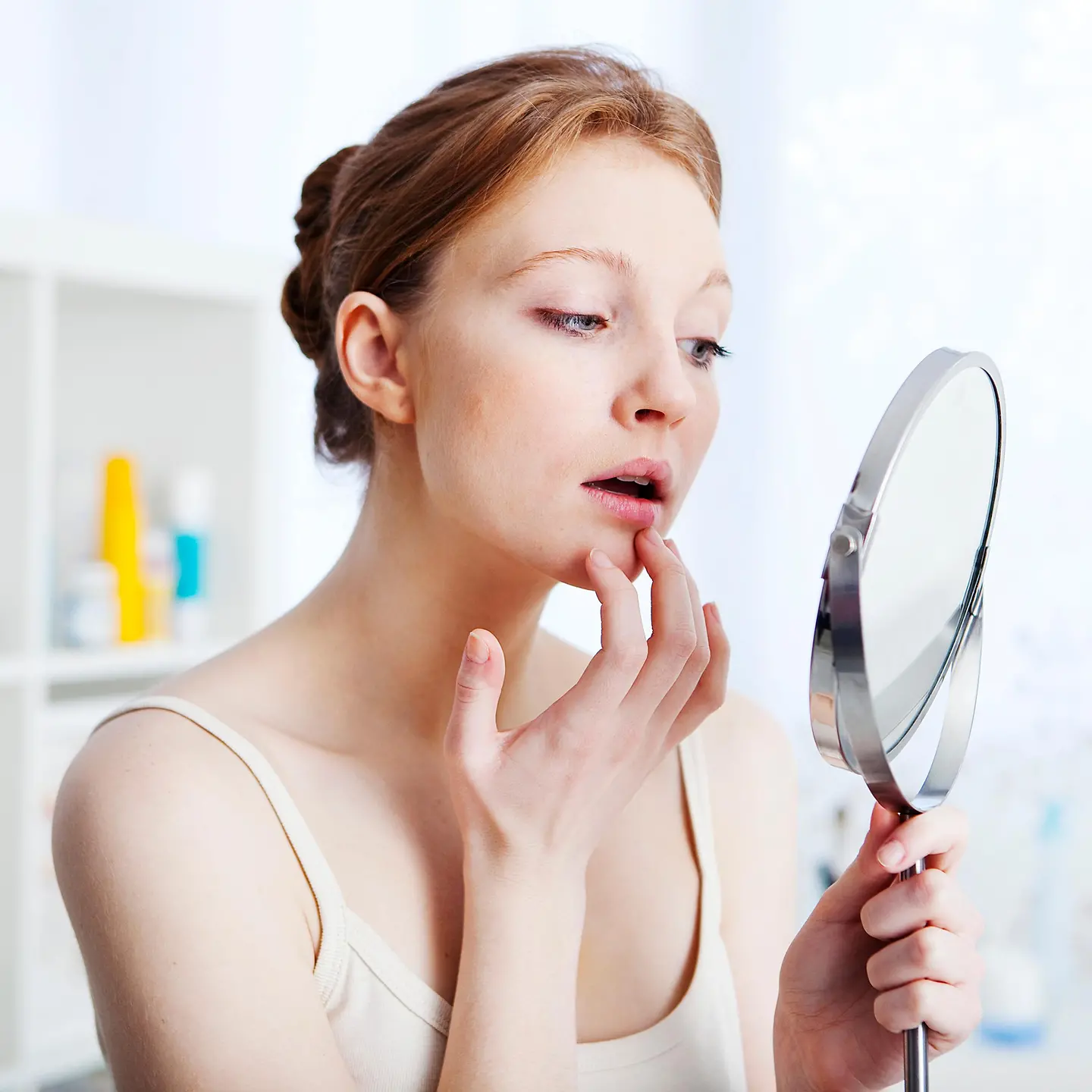 Eine Frau betrachtet sich in einem Handspiegel und fasst mit der Hand an ihre Unterlippe. Sie sieht besorgt aus. 
