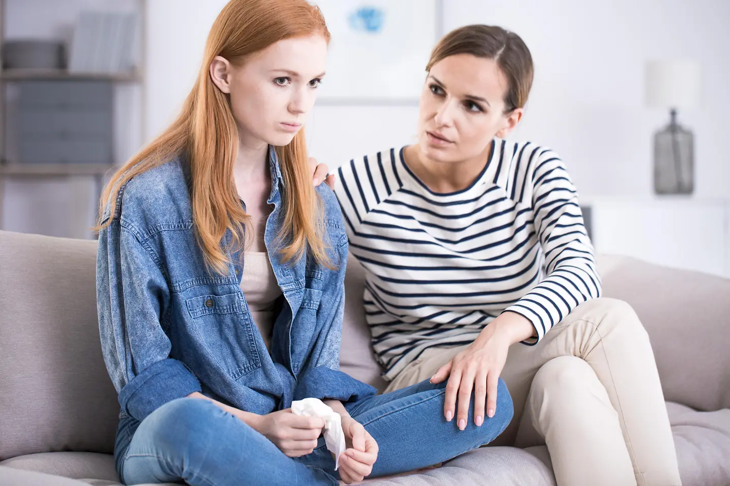 Ein junges, trauriges und sehr dünnes Mädchen mit Taschentuch in der Hand sitzt mit ihrer Mutter auf dem Sofa.