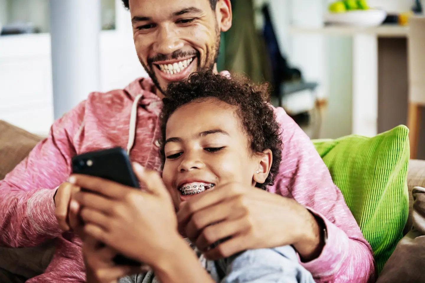 Vater und Sohn liegen auf dem Sofa und schauen lachend auf ein Smartphone
