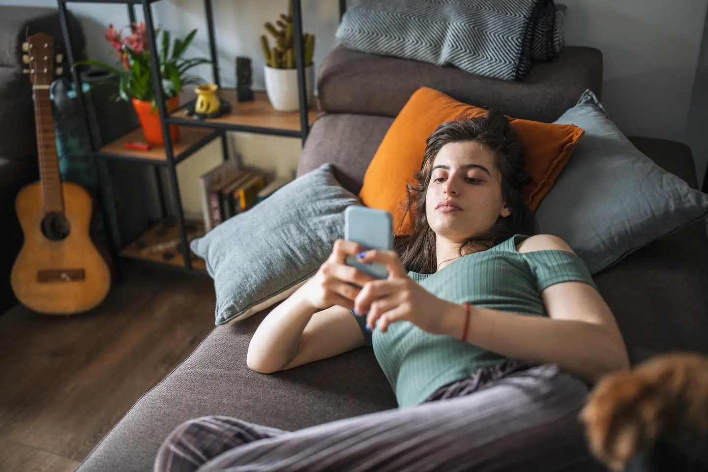 Junge Frau liegt mit ihrem Handy auf einer Couch