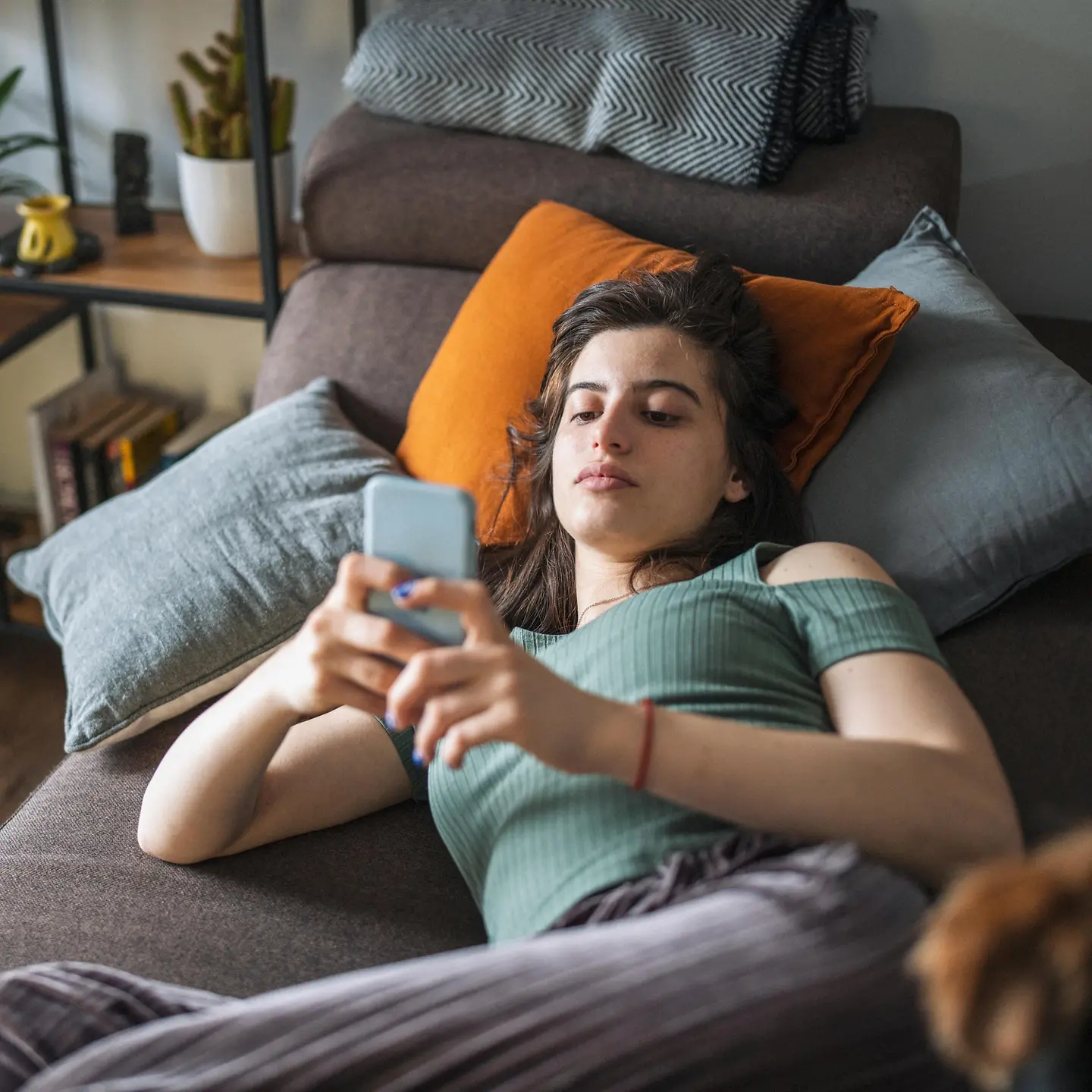 Junge Frau liegt mit ihrem Handy auf einer Couch