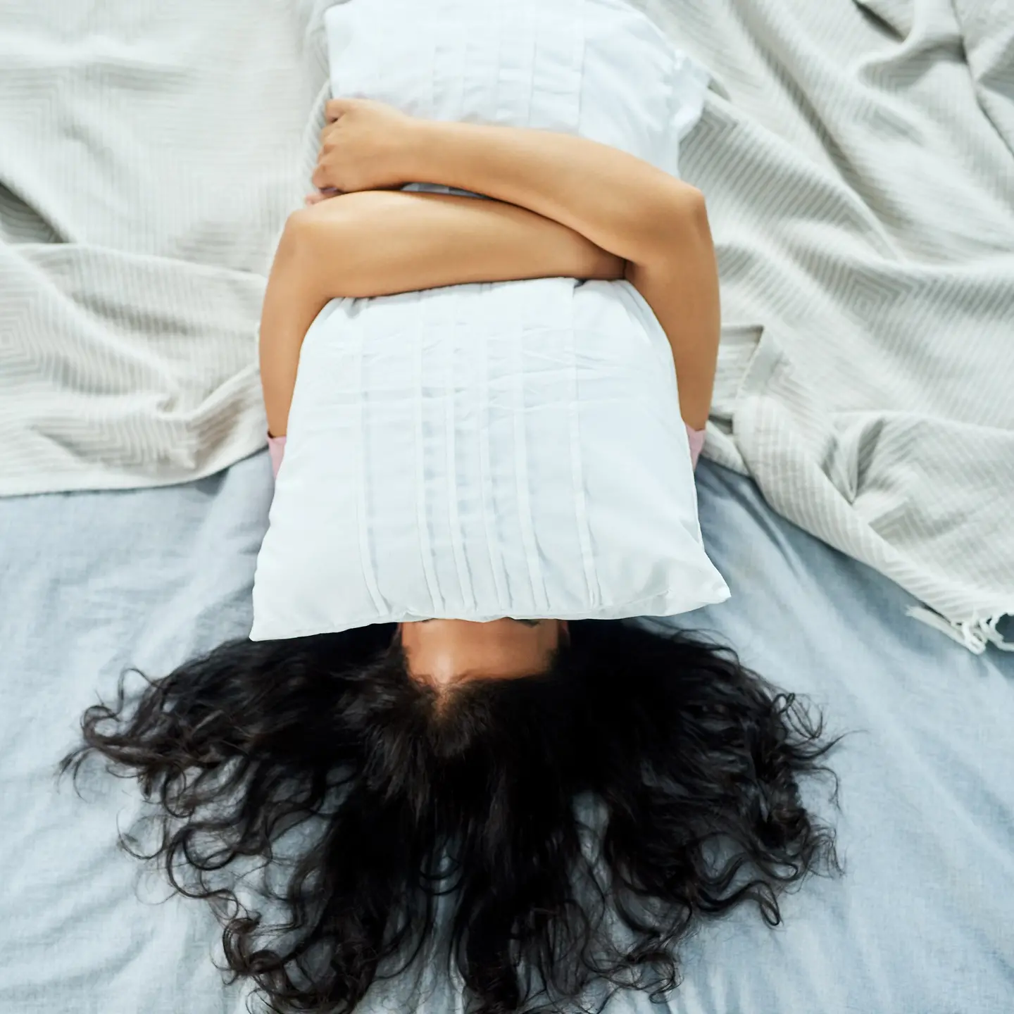 Frau liegt im Bett und hält sich ein Kissen vor ihr Gesicht