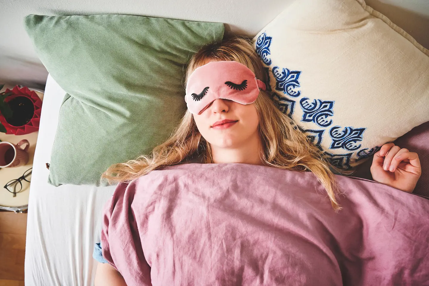 Junge Frau mit Schlafmaske liegt im Bett