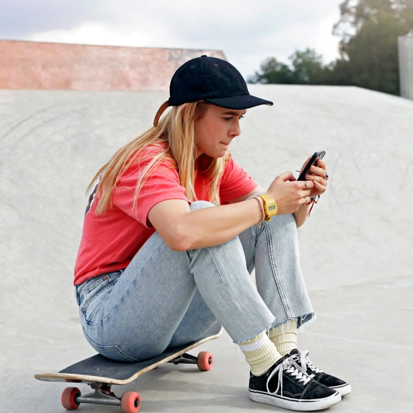 Ein Mädchen sitzt auf einem Skateboard und schaut auf ihr Handy