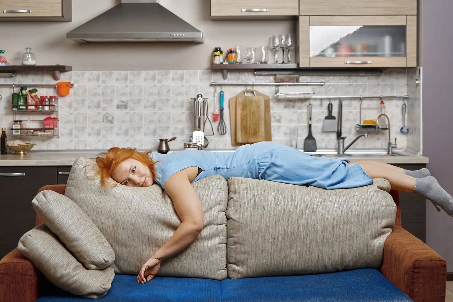Eine junge Frau liegt erschöpft auf der Rückenlehne einer Couch