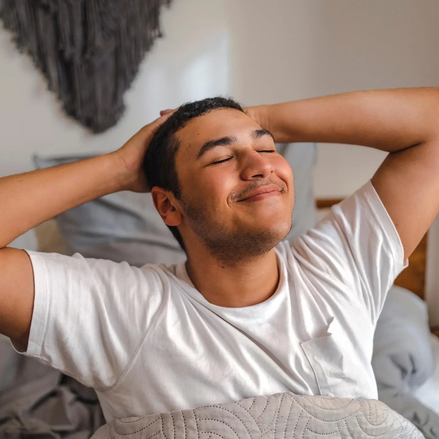 Ein junger Mann sitzt in seinem Bett und streckt sich