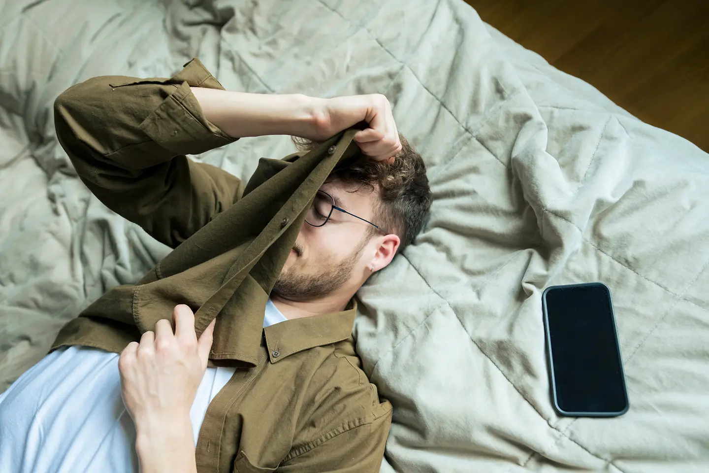 Ein müder junger Mann liegt neben seinem Smartphone auf seinem Bett