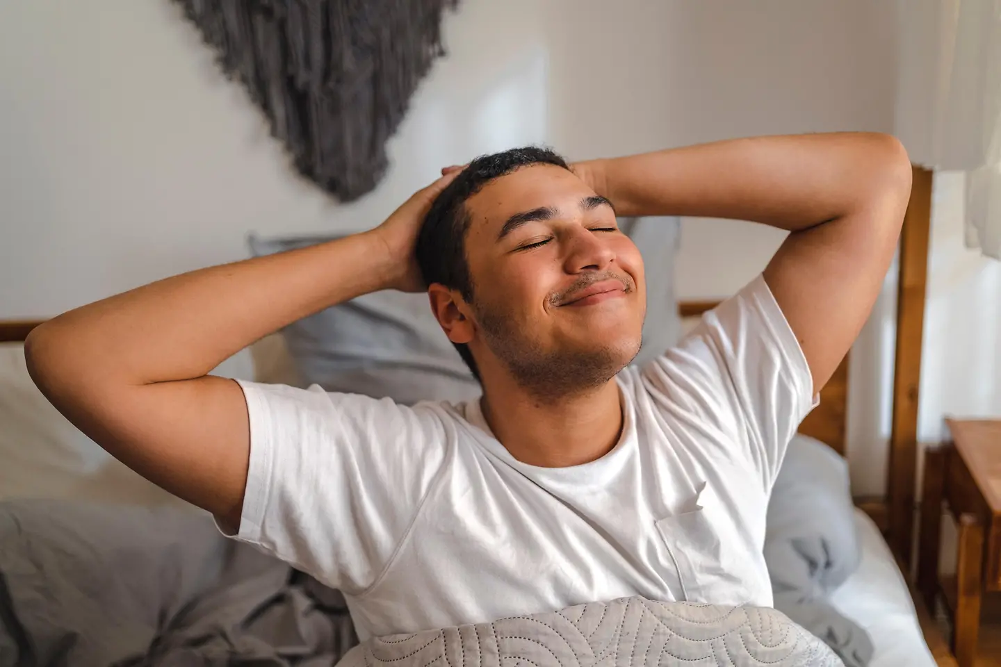 Ein junger Mann sitzt in seinem Bett und streckt sich