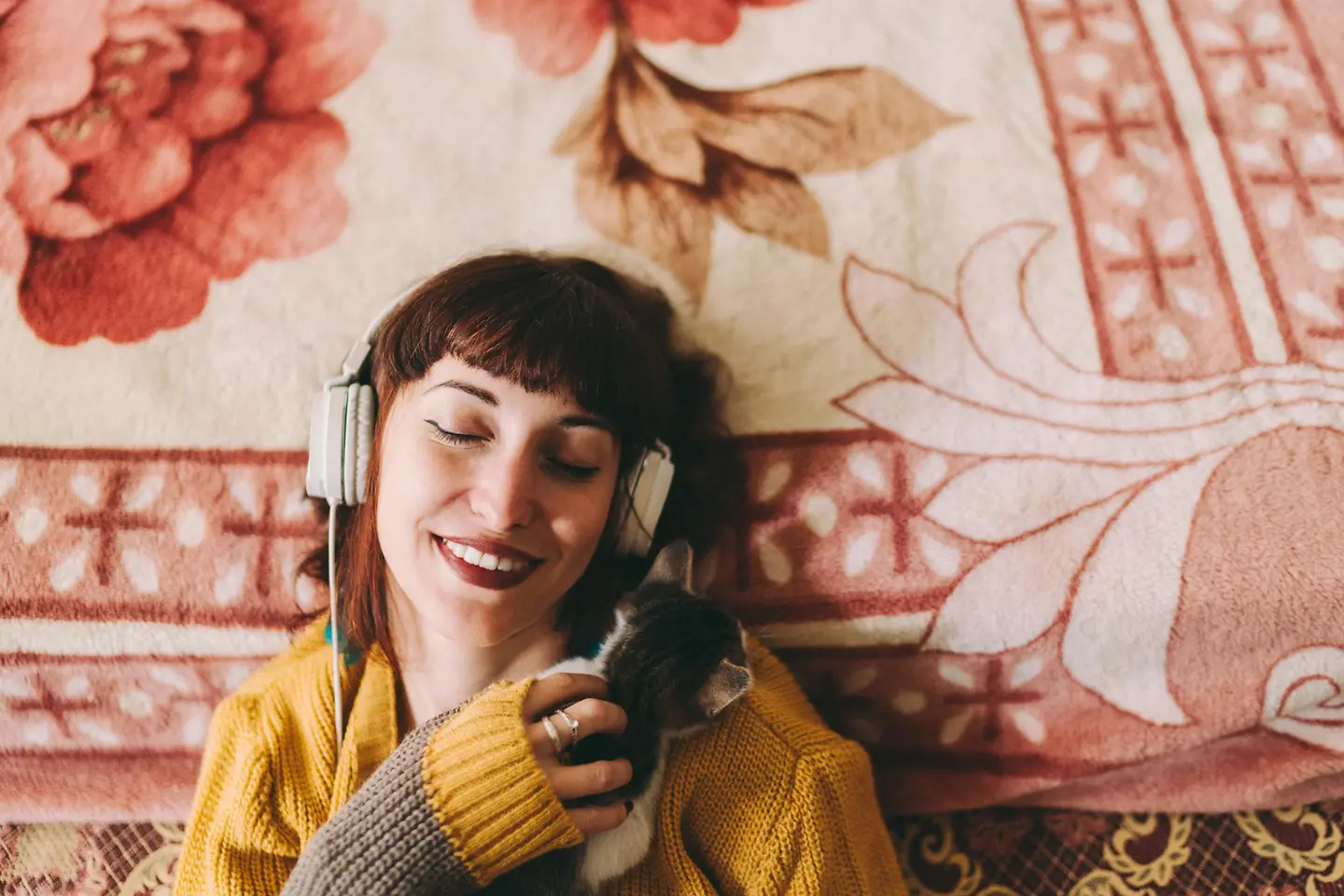 Eine jungen Frau hört Musik mit einem Kopfhörer und schmust mit einer Katze