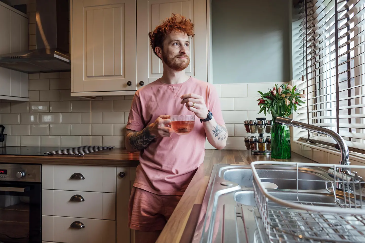 Ein junger rothaariger Mann steht in der Küche und hält eine Tasse Tee in der Hand
