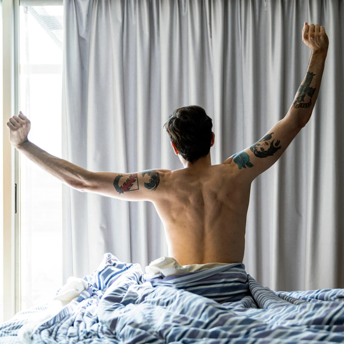 Rückansicht eines Mannes, der sich im Bett aufsetzt und streckt