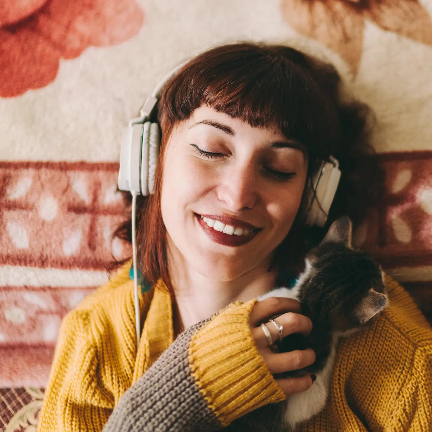 Eine jungen Frau hört Musik mit einem Kopfhörer und schmust mit einer Katze