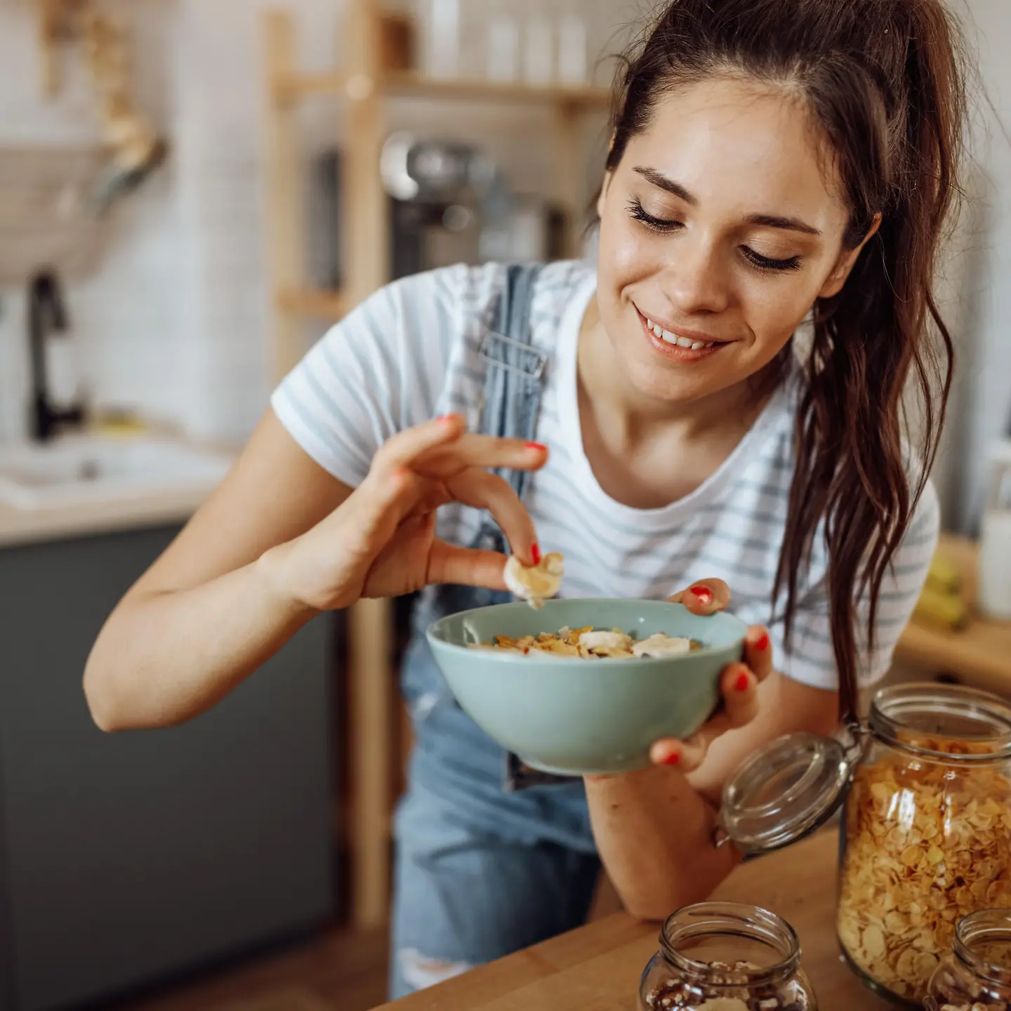 Eine junge Frau mit Pferdeschwanz nimmt ein Stück Banane aus einer blauen Schüssel mit Müsli.