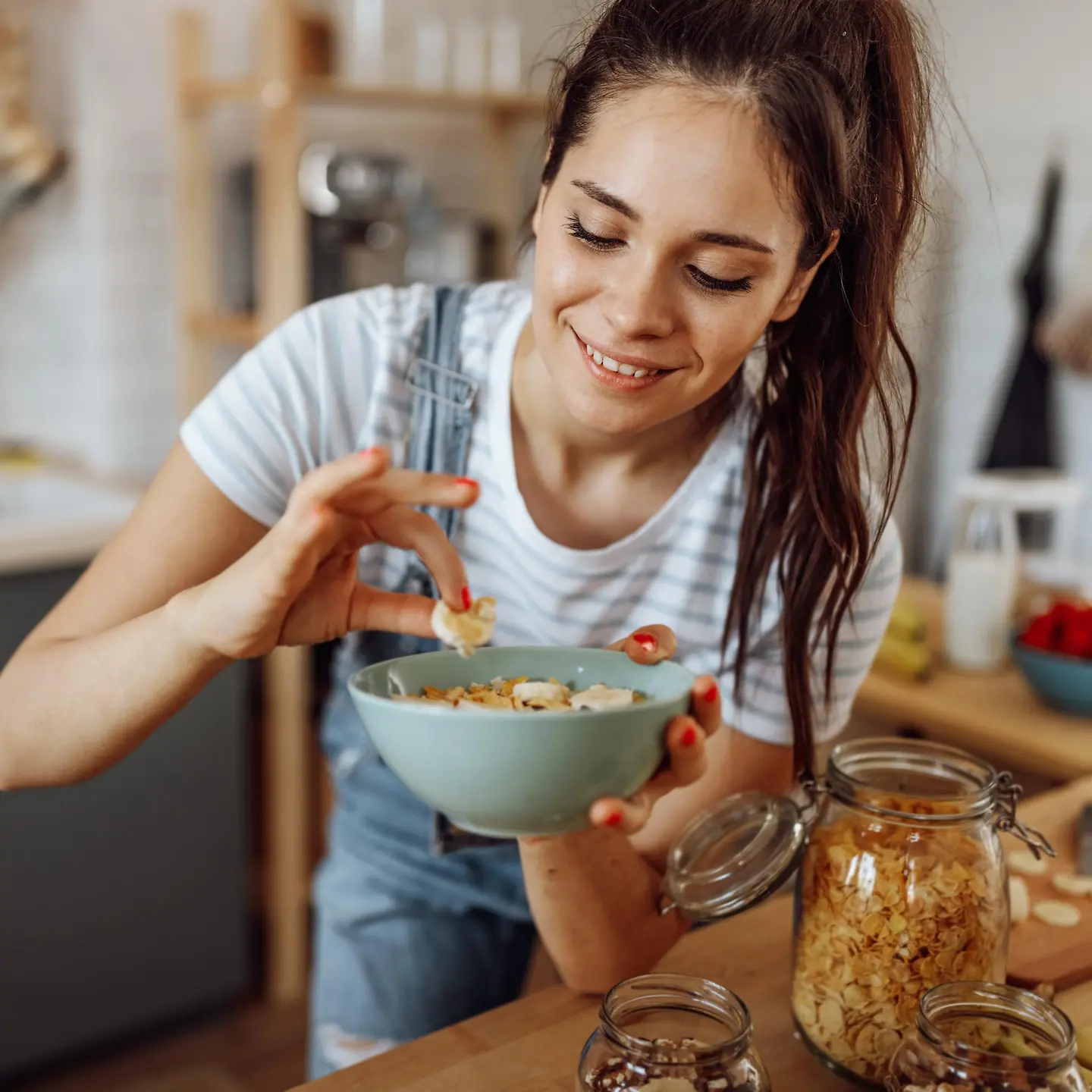 Eine junge Frau mit Pferdeschwanz nimmt ein Stück Banane aus einer blauen Schüssel mit Müsli.