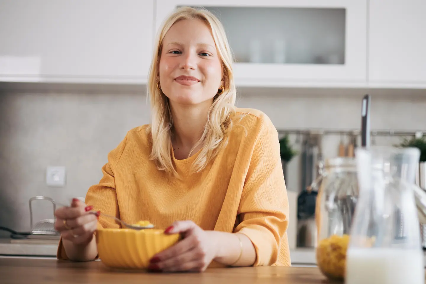 Junge, blonde Frau genießt ihr Frühstücksmüsli in der Küche