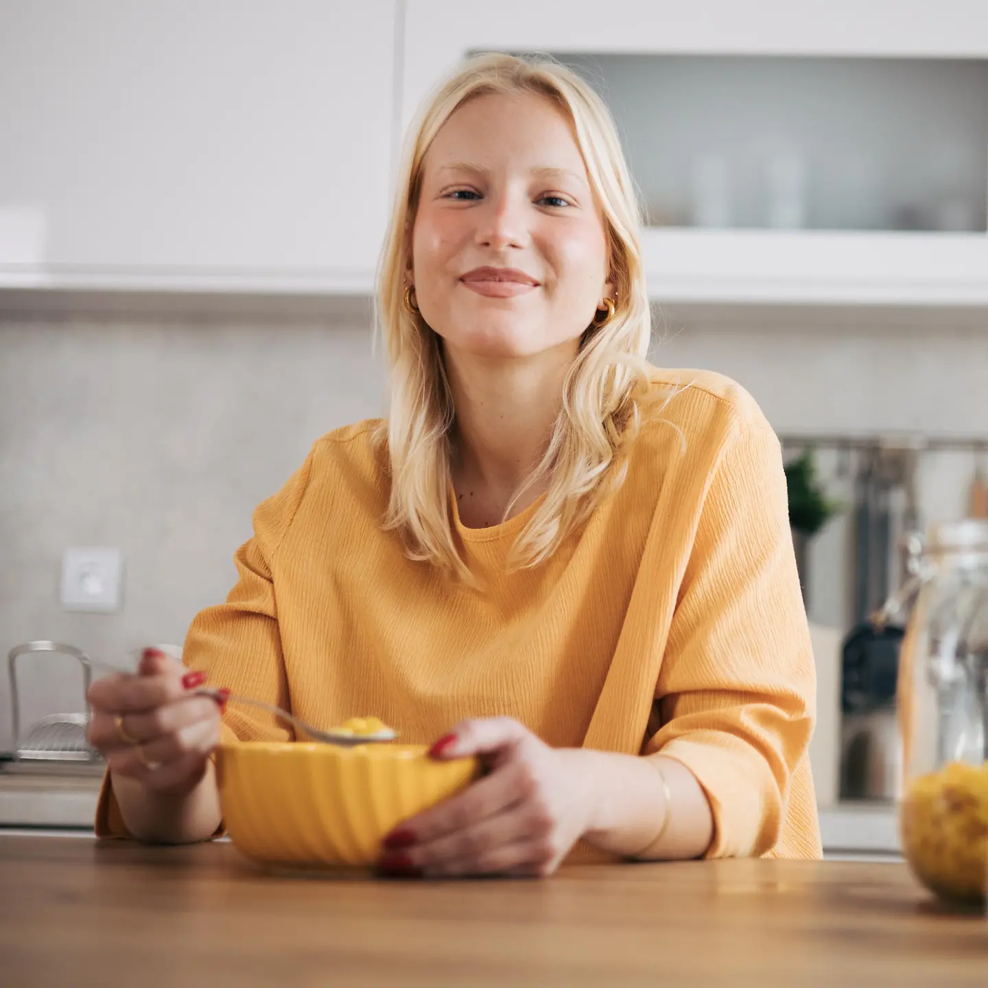 Junge, blonde Frau genießt ihr Frühstücksmüsli in der Küche