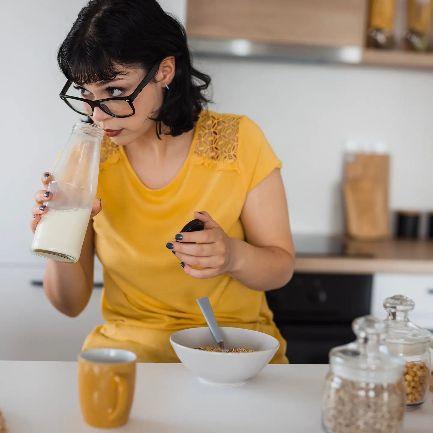 Eine Frau steht in der Küche und riecht an einer Flasche Milch.