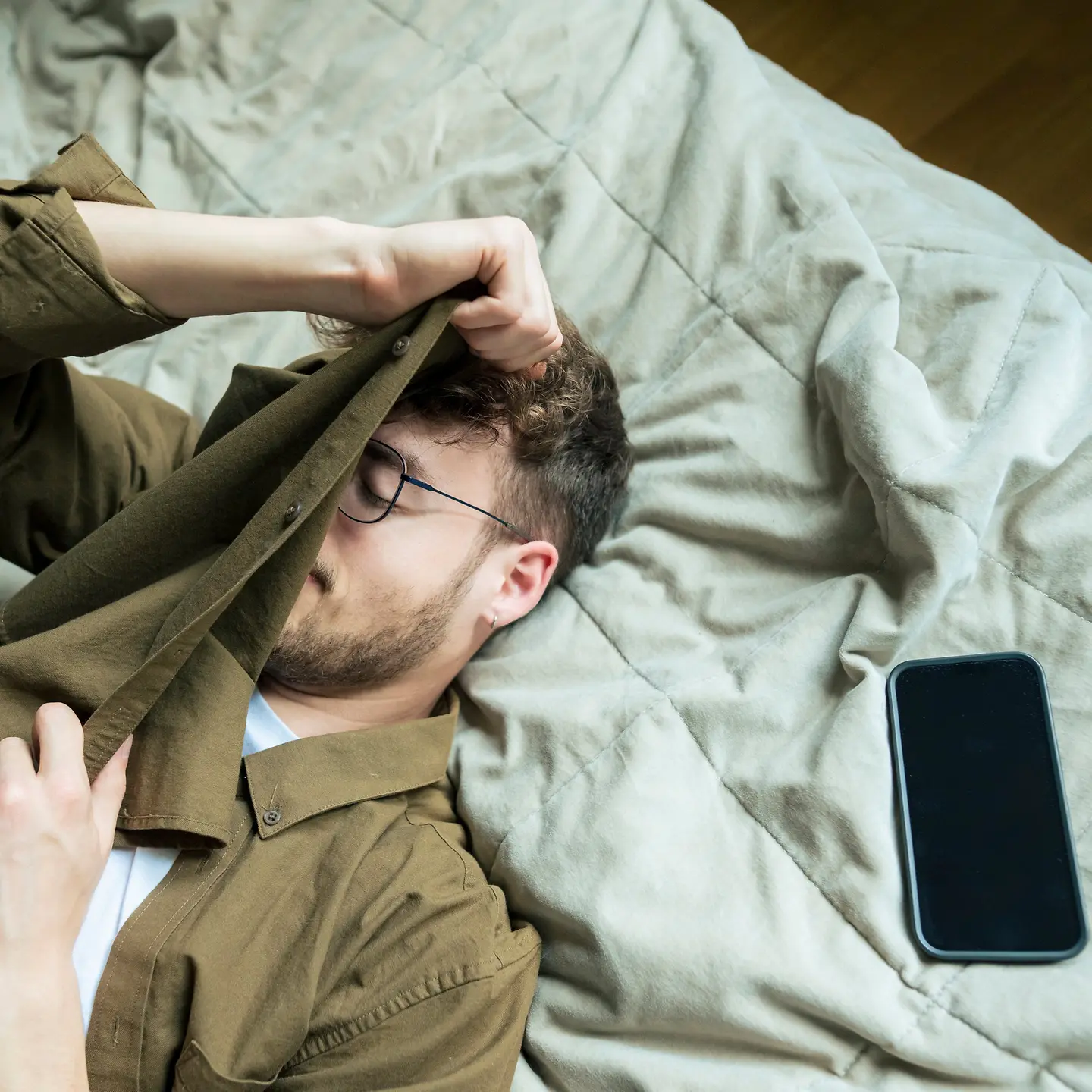 Ein müder junger Mann liegt neben seinem Smartphone auf seinem Bett