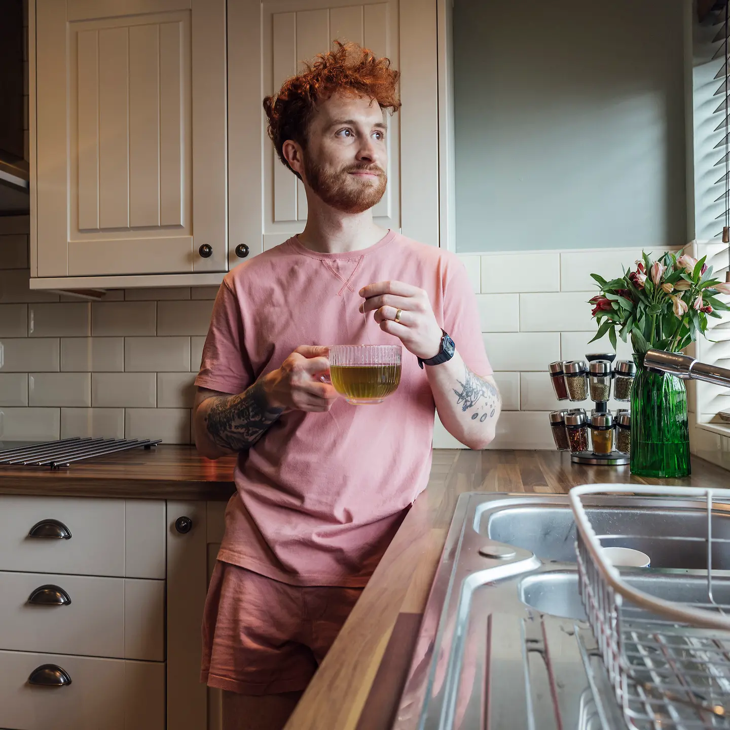 Ein junger rothaariger Mann steht in der Küche und hält eine Tasse Tee in der Hand