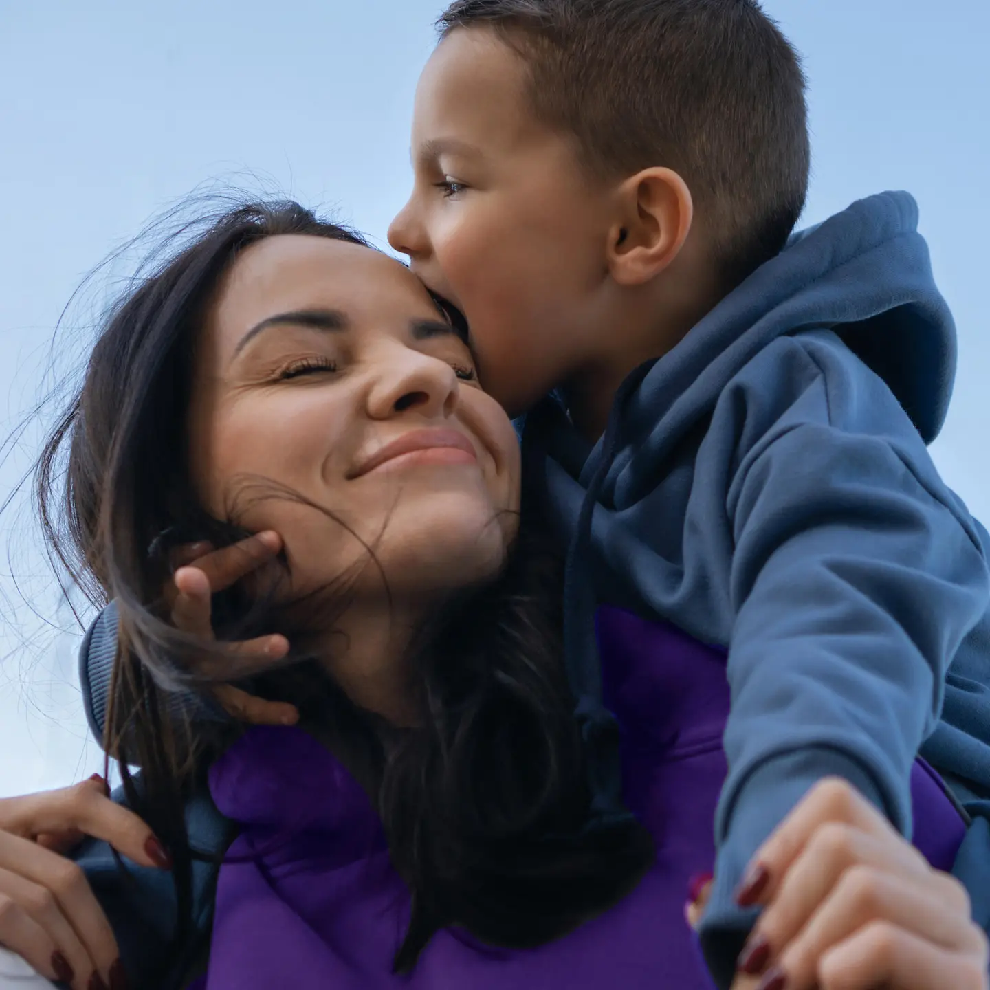 Eine Mutter mit ihrem Sohn auf den Schultern vor blauem Himmel