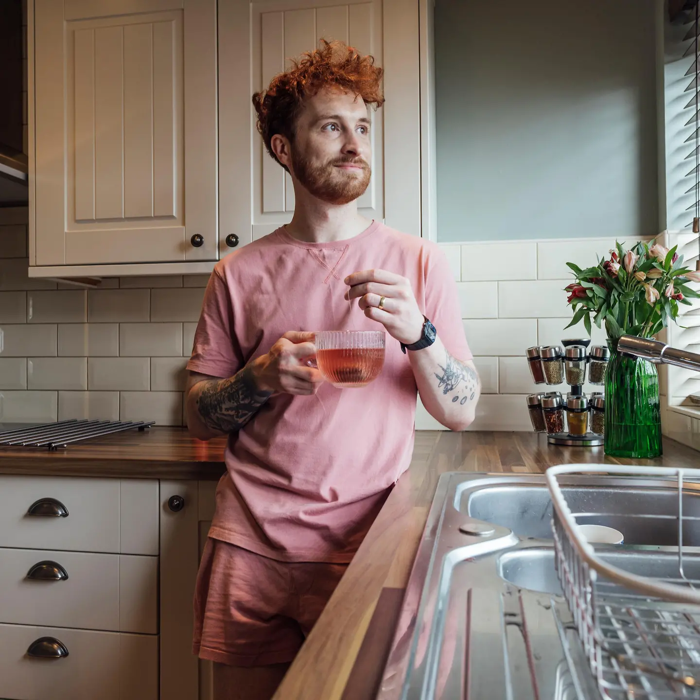 Ein junger rothaariger Mann steht in der Küche und hält eine Tasse Tee in der Hand