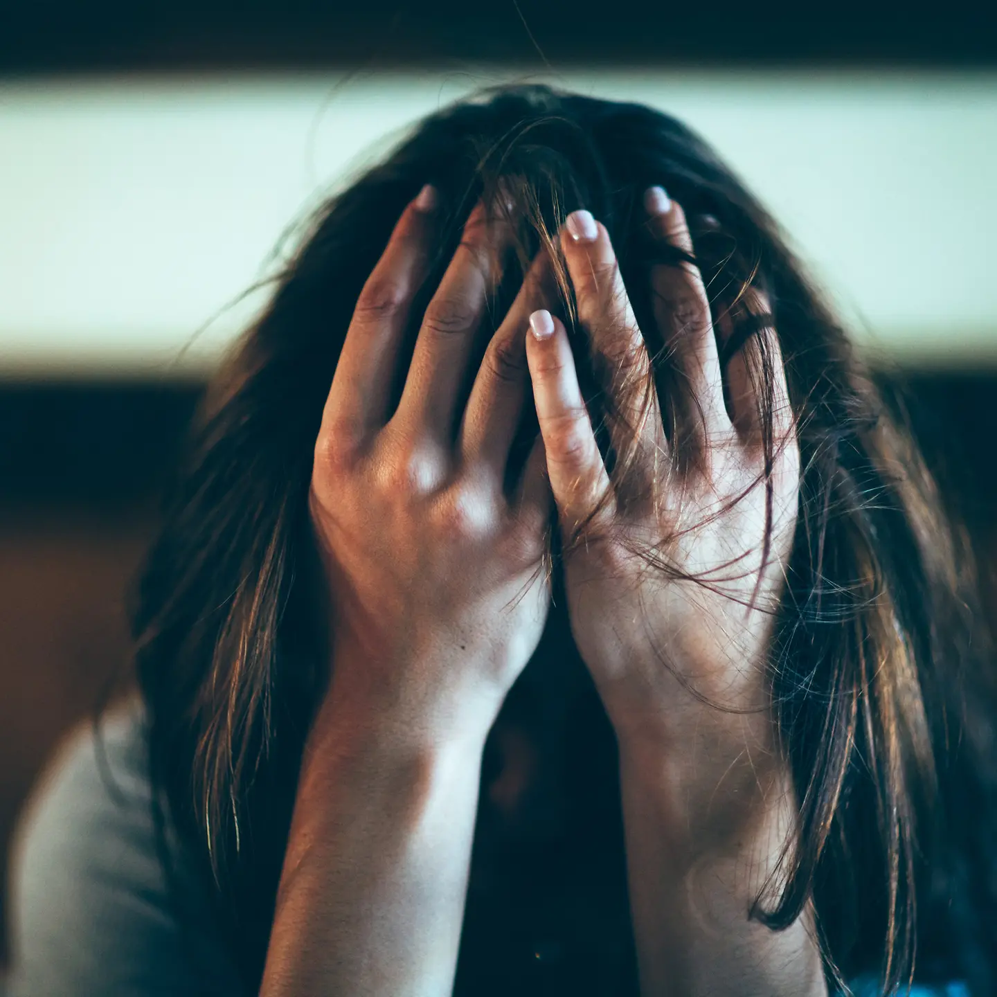 Eine Frau sitzt am Boden und hält mit beiden Händen ihr Gesicht bedeckt.