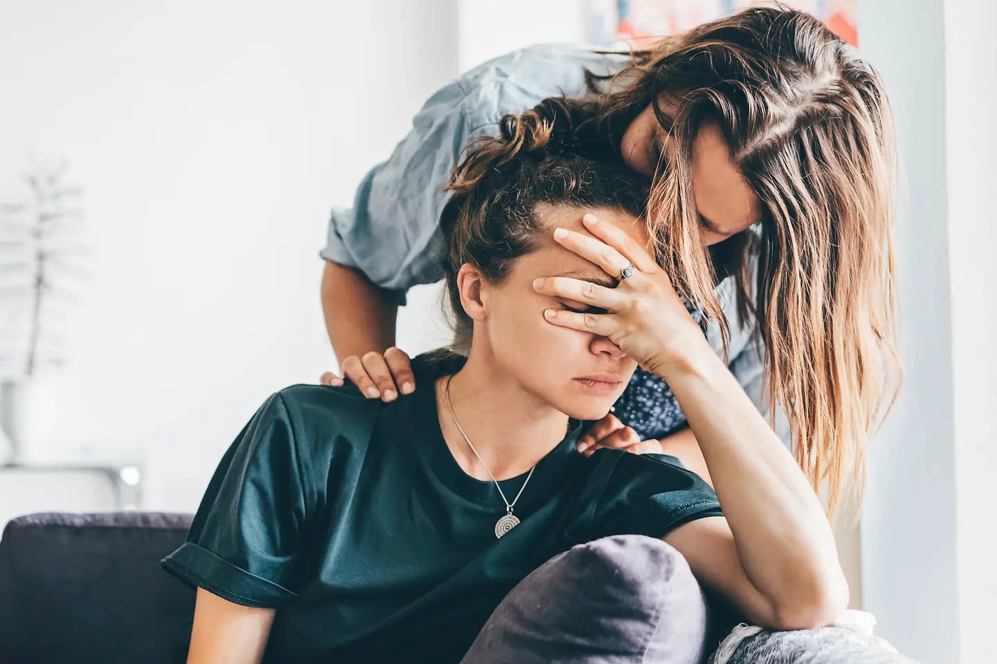 Eine Frau beugt sich über ihre Partnerin, die sich die Hand vors Gesicht hält