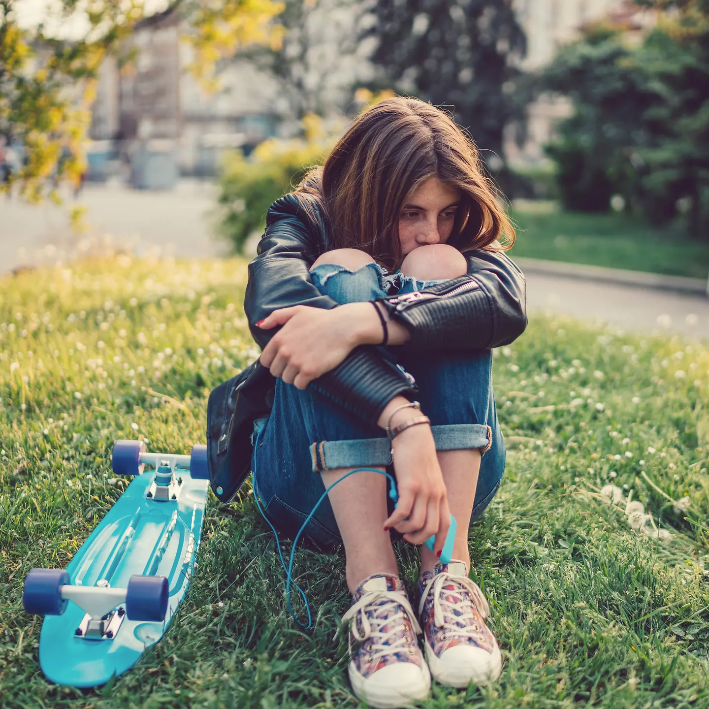 Eine junge Frau mit Weltschmerz sitzt mit einem Skateboard auf einer Wiese