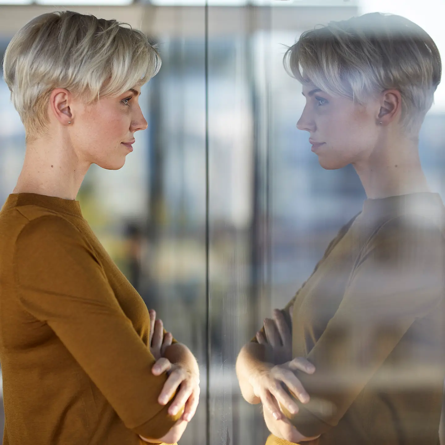 Impostor-Syndrom: Eine junge Frau mit Selbstzweifeln betrachtet ihre Reflektion in einem Fenster