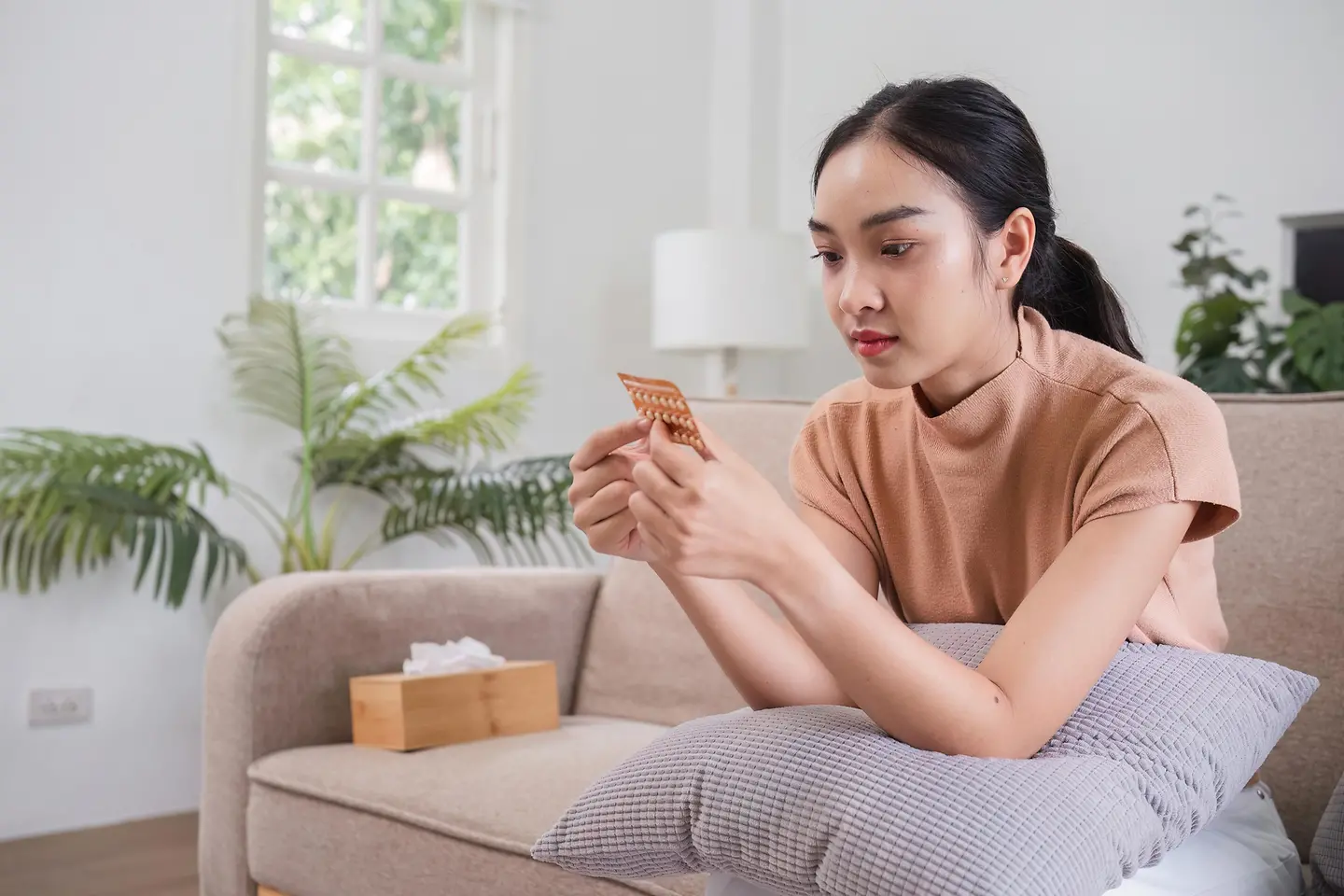 Eine junge Frau sitzt auf einer Couch und sieht sich eine Pillenpackung an