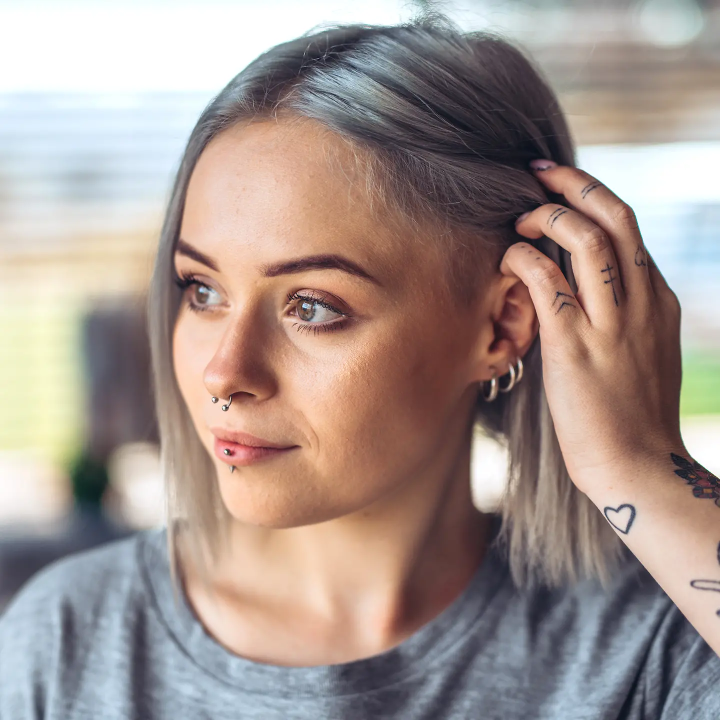 Junge Frau mit drei Ohrringen und Tattoo am Arm streift sich die Haare hinter das linke Ohr