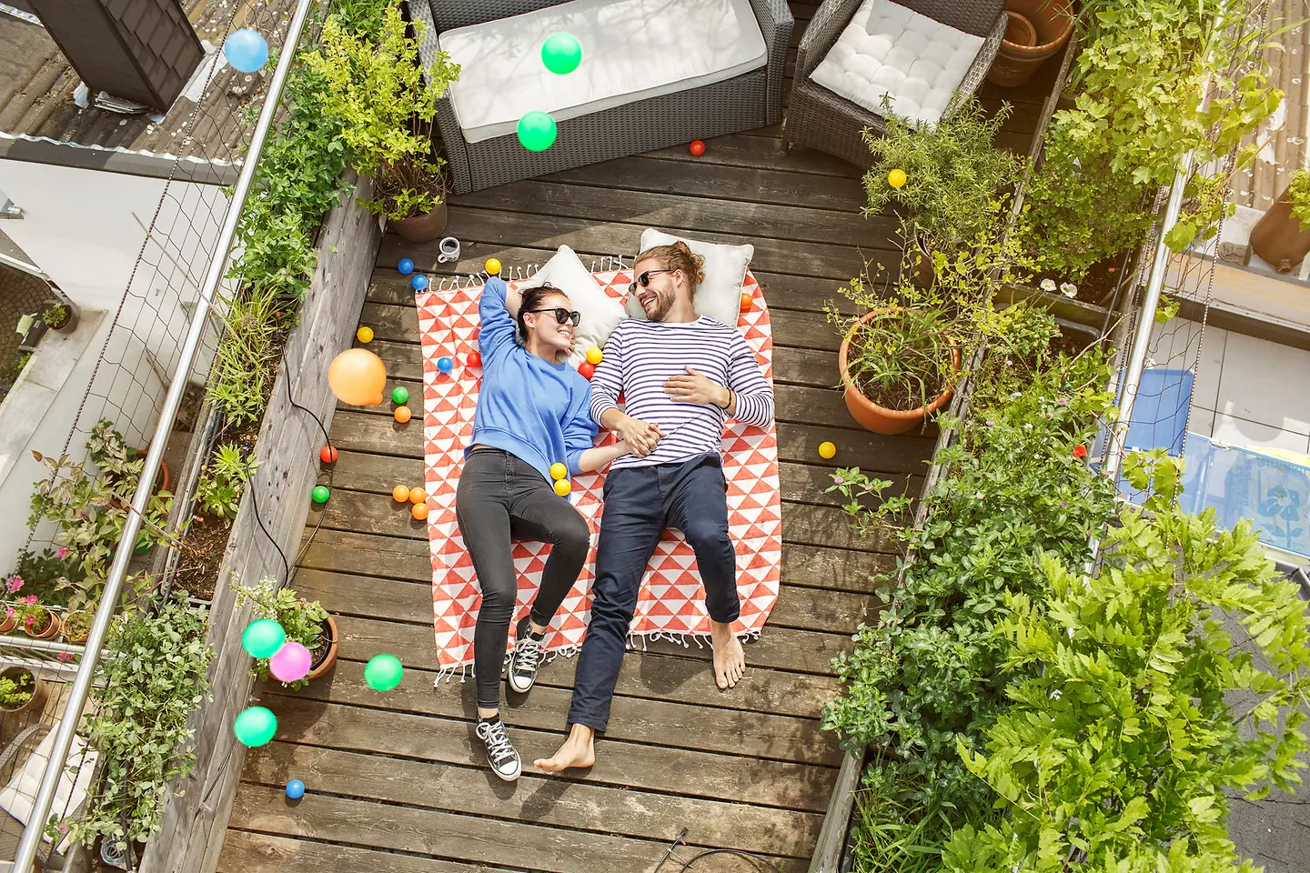 Ein junges Paar liegt lachend auf einem Balkon mit Holzdielen