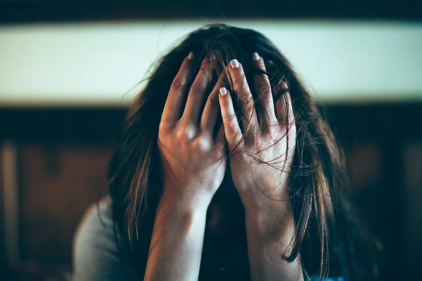 Eine Frau sitzt am Boden und hält mit beiden Händen ihr Gesicht bedeckt.