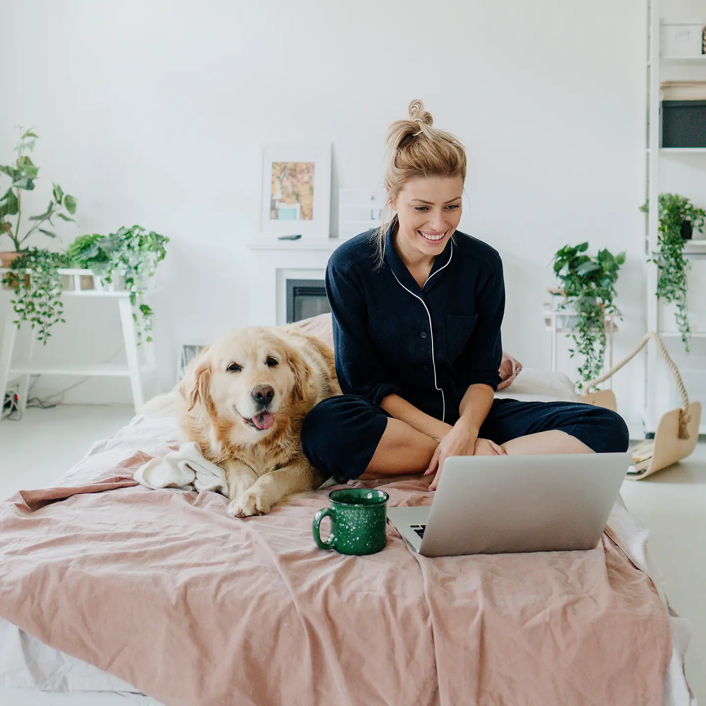 Eine Frau sitzt im Schlafanzug mit Notebook und Hund auf dem Bett